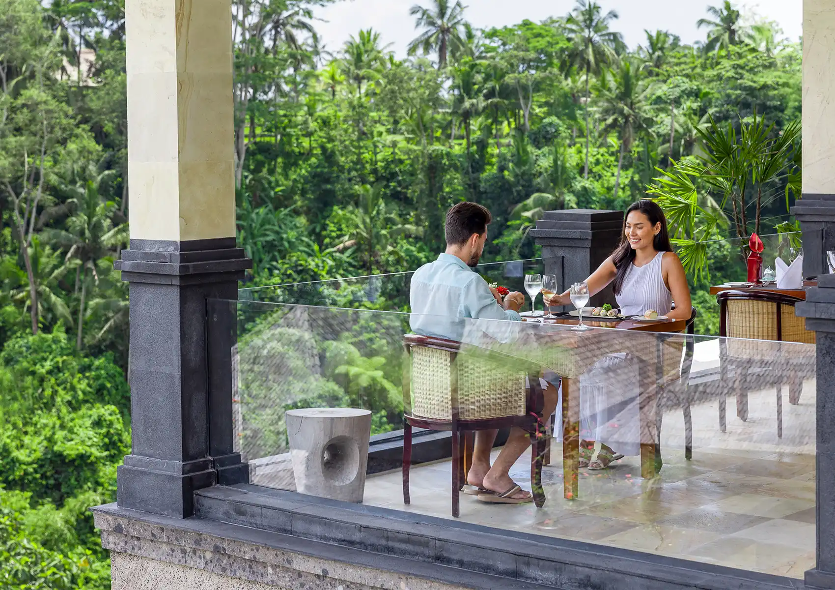Romantic dinner Ubud balcony with couple dining above lush tropical forest and palm trees.