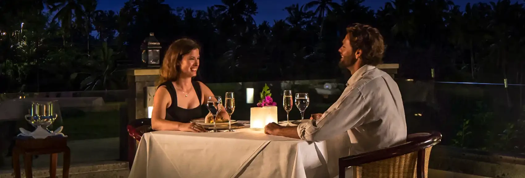 Elegant outdoor dining in Ubud with woman in white dress and man enjoying drink amid lush tropical greenery.