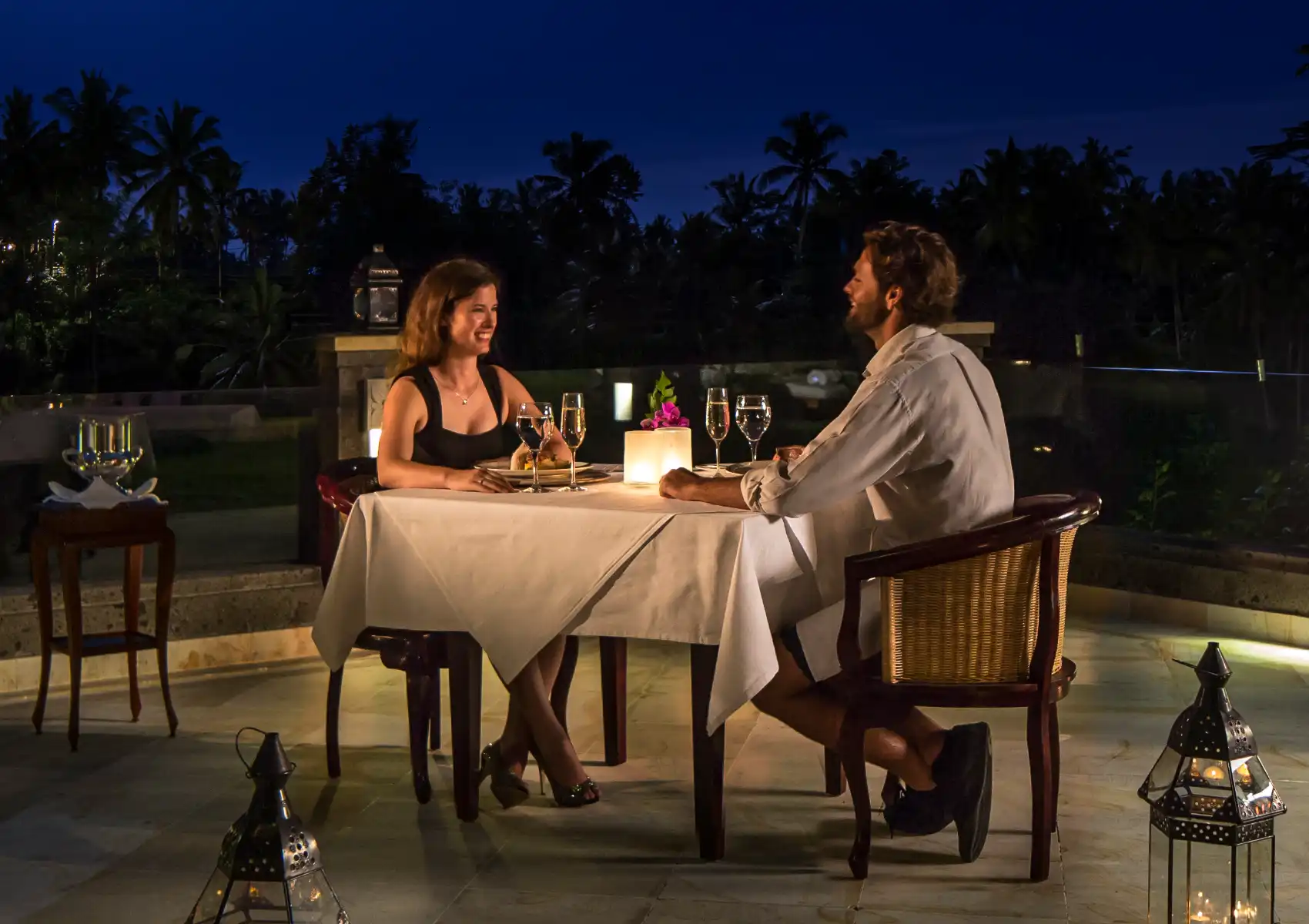 Elegant outdoor dining in Ubud with woman in white dress and man enjoying drink amid lush tropical greenery.