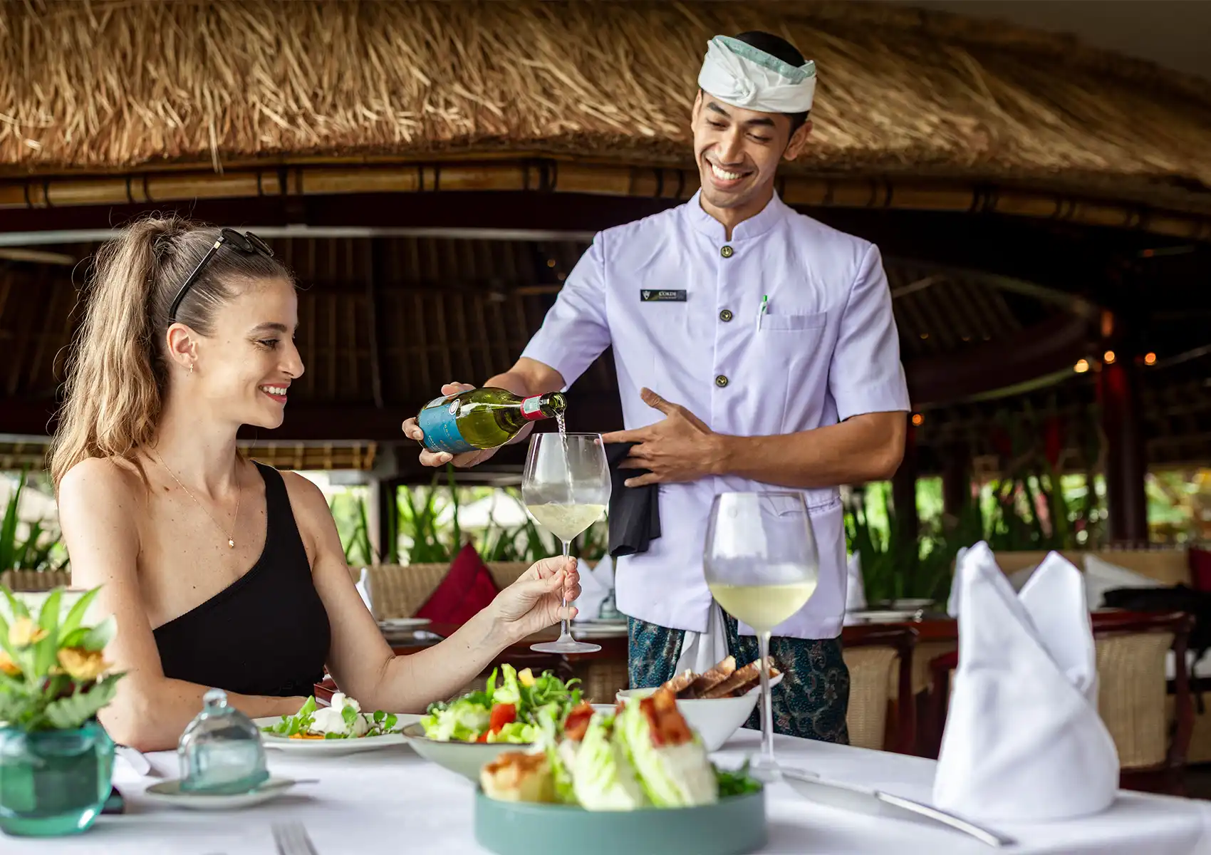 Server pouring white wine at fine dining table in Ubud with tropical open‑air setting and attentive service.