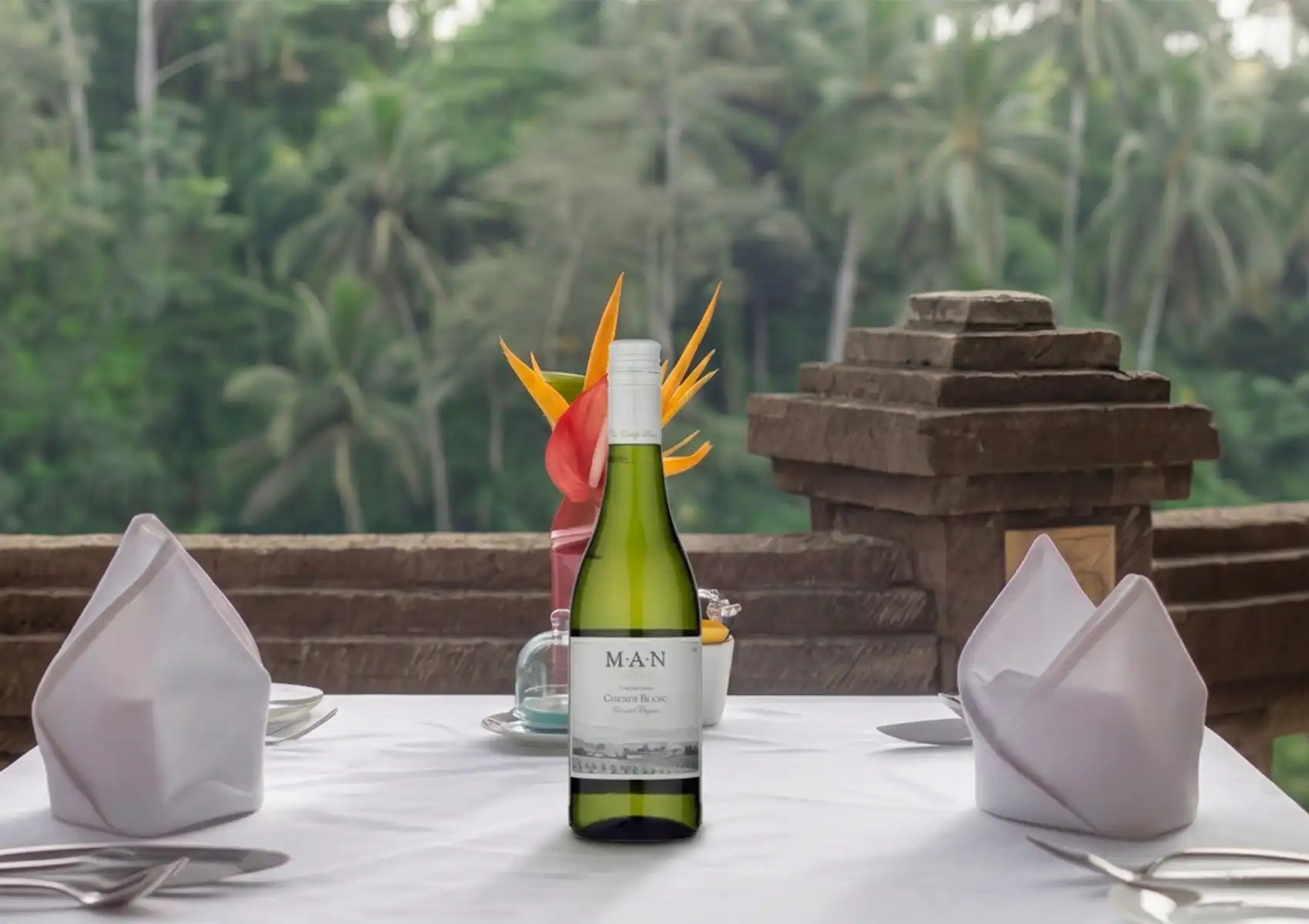 Outdoor fine dining table with wine and tropical flowers overlooking lush forest in Ubud.