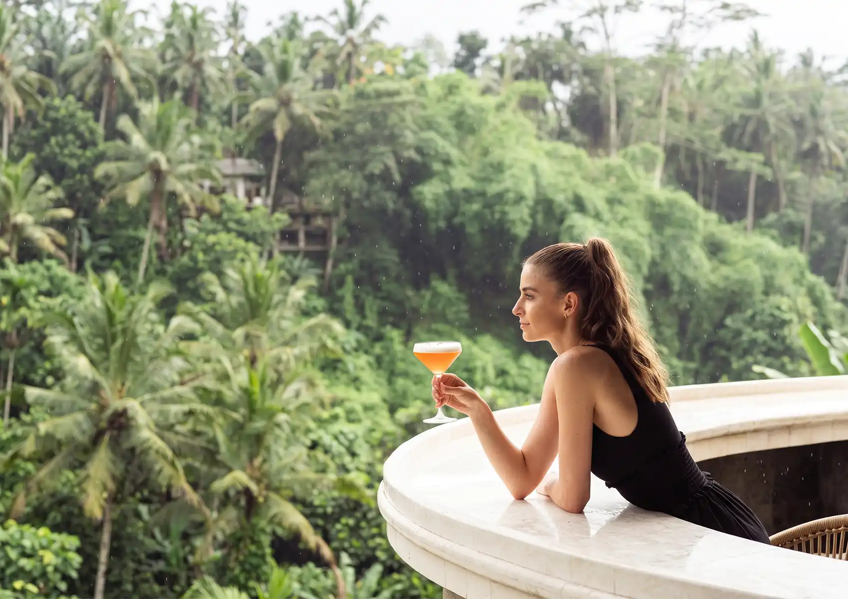 Woman sipping a signature cocktail on a jungle-view terrace bar in Ubud Bali overlooking the lush valley.