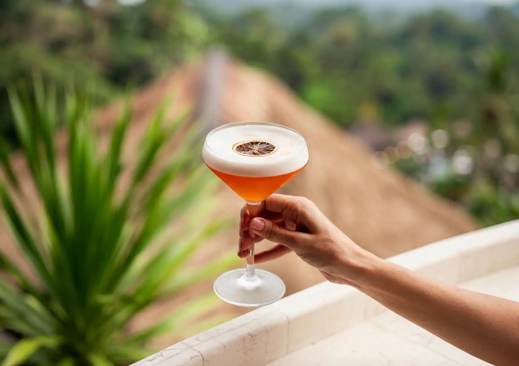 Signature cocktail CasCades served on an open-air terrace overlooking the lush jungle valley in Ubud, Bali.