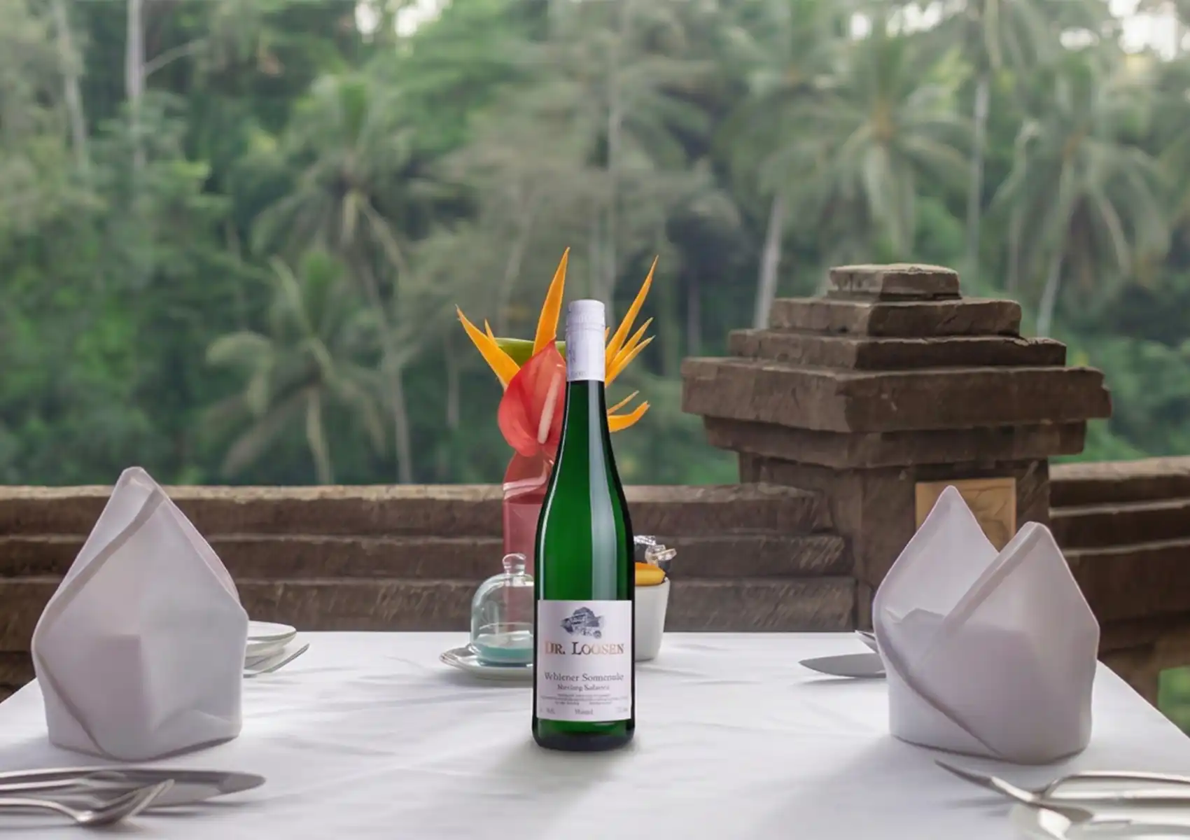 Outdoor restaurant in Ubud with elegant table setting, tropical flowers, and terrace view of palm forest.