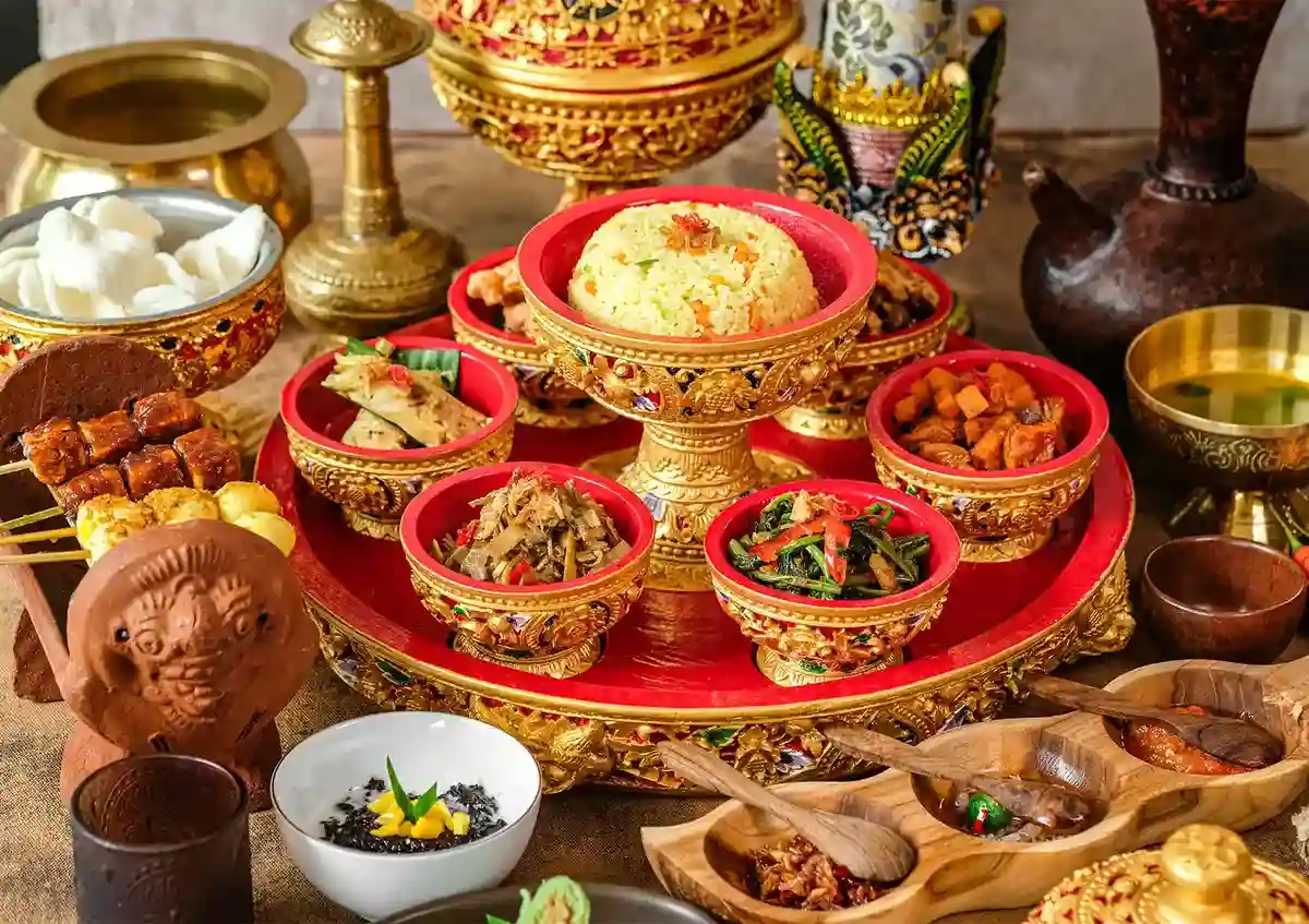 Balinese ceremonial feast with yellow rice, satay skewers, and side dishes in ornate golden bowls.