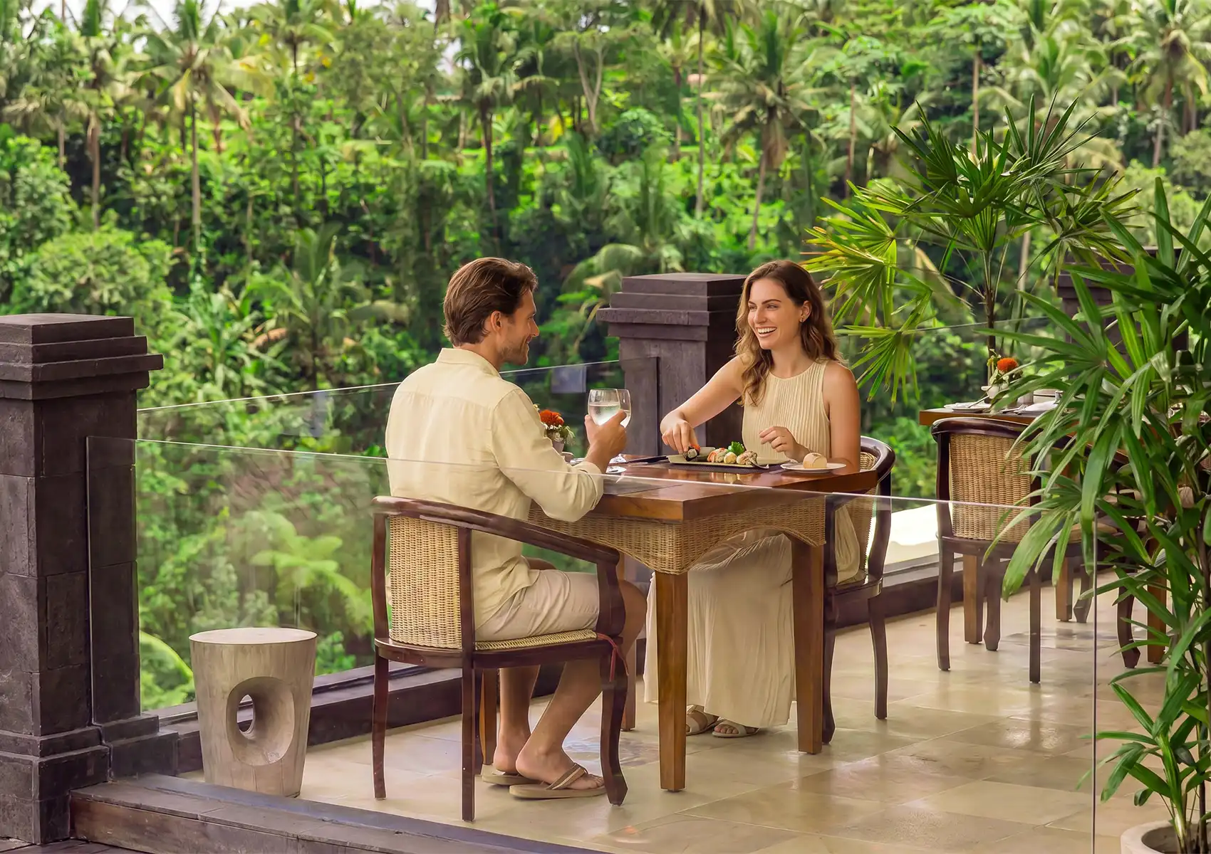 A smiling couple enjoying a romantic meal and drinks at a scenic outdoor table overlooking the beautiful, lush tropical jungle at a restaurant in ubud.