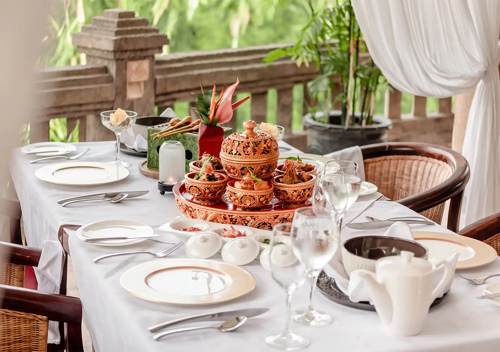 An elegantly set table on a balcony overlooking lush greenery, featuring a traditional Balinese culinary centerpiece at a fine dining restaurant in Ubud.
