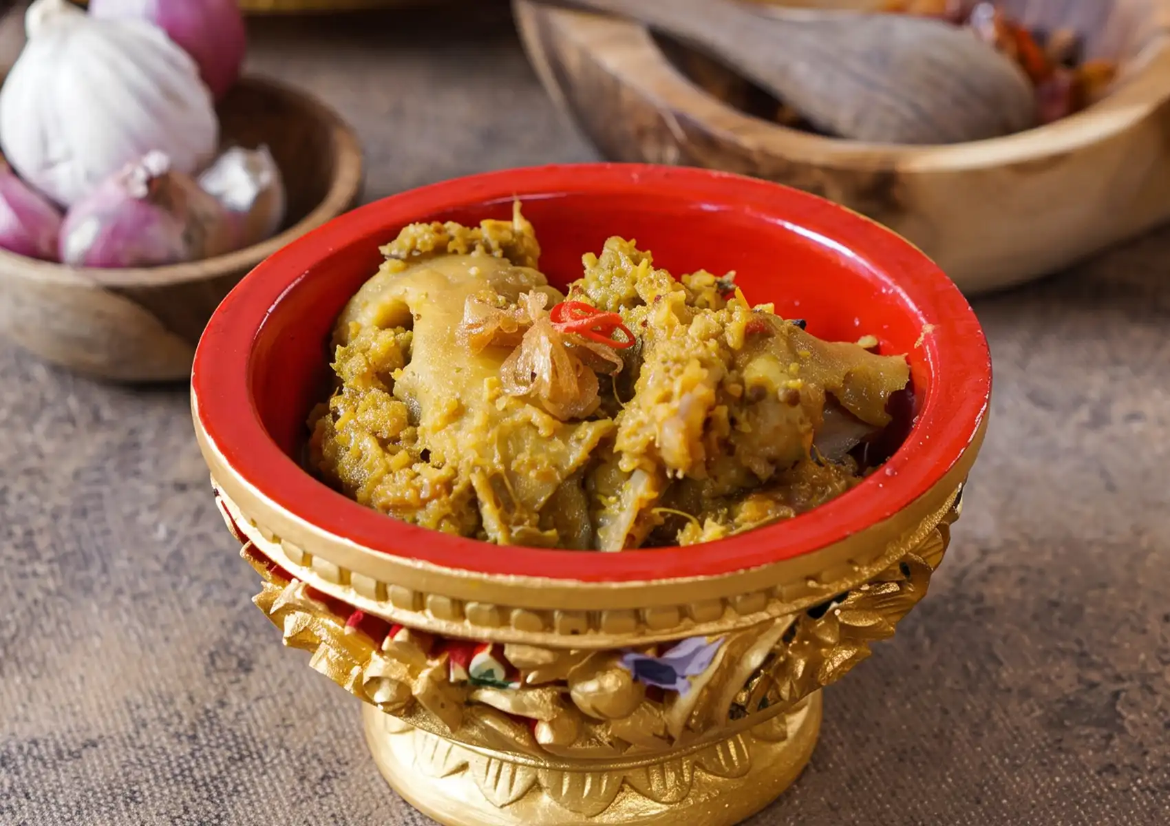 A close-up of Bebek Betutu, a traditional spiced dish, served in an ornate gold and red bowl at a restaurant in Ubud.