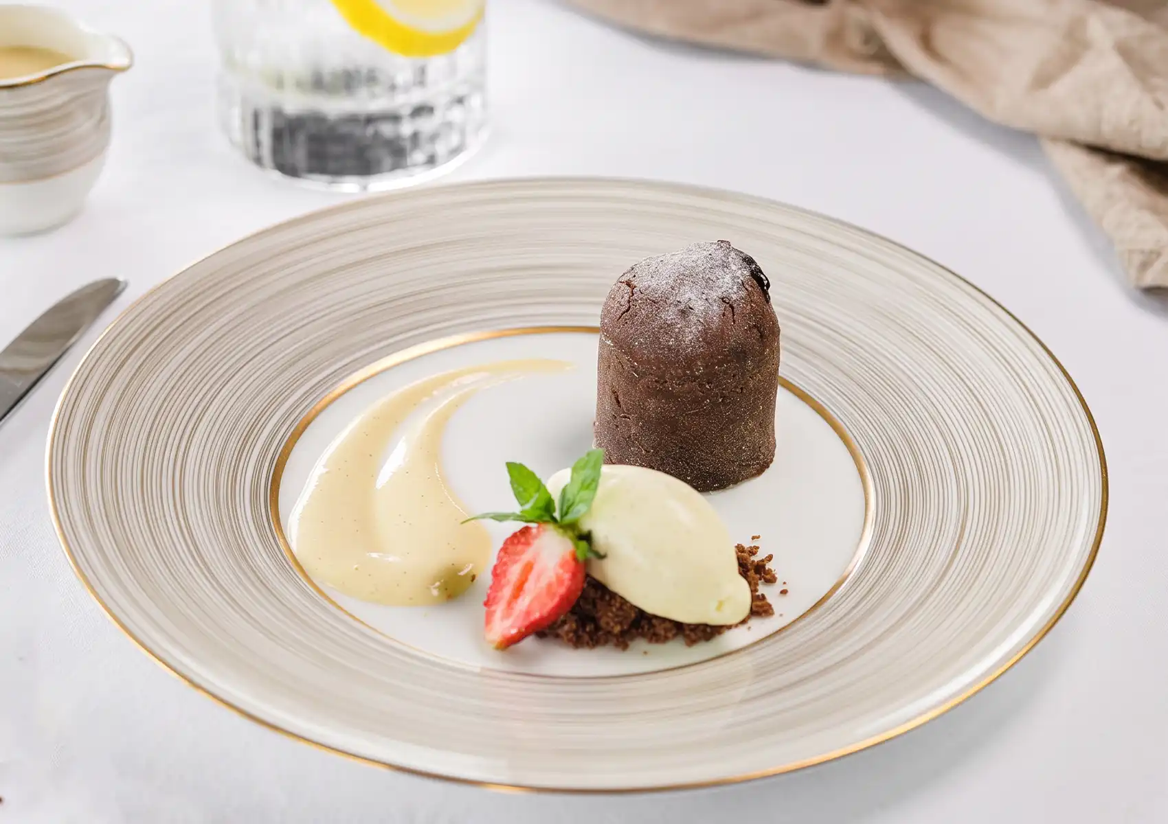 A chocolate fondant dessert served with a scoop of vanilla ice cream, a fresh strawberry, and a sweet sauce smear on an elegant plate at a restaurant in Ubud.