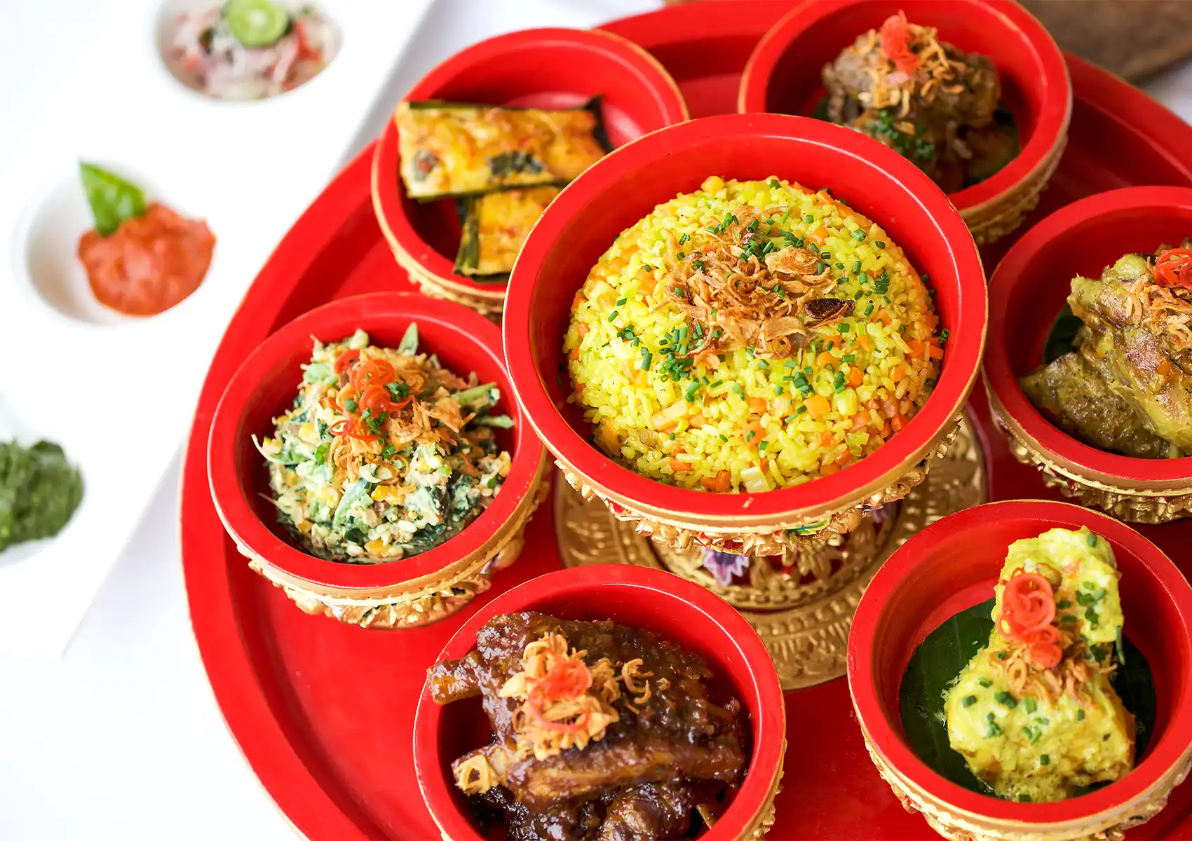 Close-up of a vibrant traditional Balinese meal featuring yellow rice and various side dishes in red tiered bowls, served at a restaurant romantic Ubud.