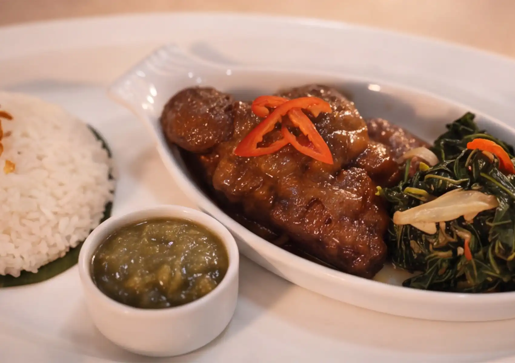 A close-up view of tender, slow-cooked beef rendang garnished with sliced red chili, accompanied by green sambal and mixed vegetables at a Restaurant in ubud.