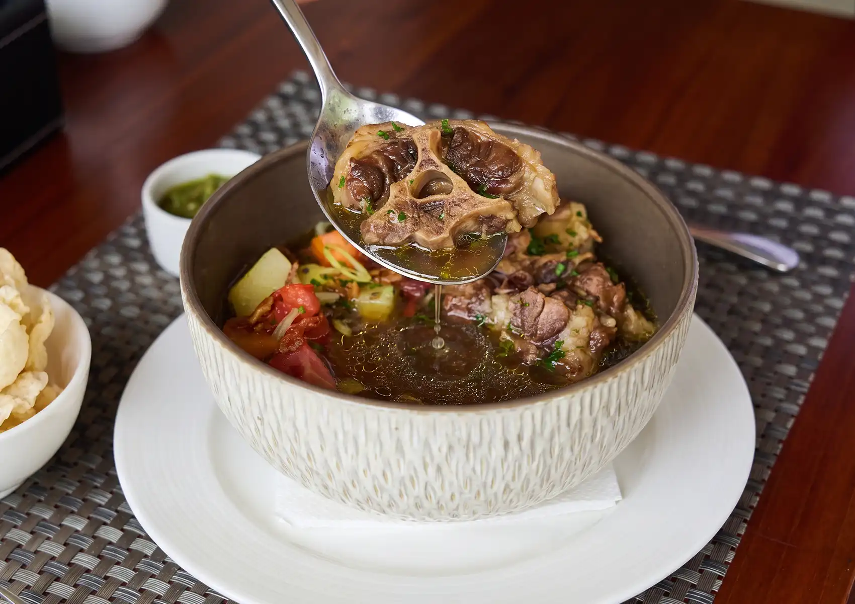 A close-up of a spoon lifting a tender, bone-in piece of meat from a rich bowl of authentic Indonesian oxtail soup at a Restaurant in ubud.